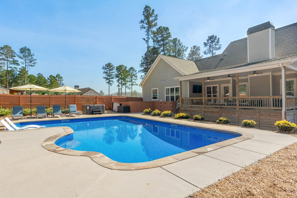 Backyard pool beside a home with a covered porch and fenced yard.