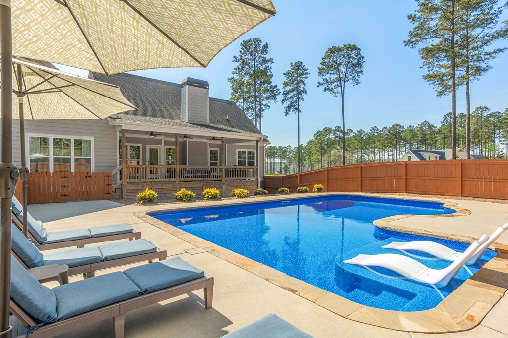 Backyard pool beside a gray-sided home, with lounge chairs and white in-pool loungers.
