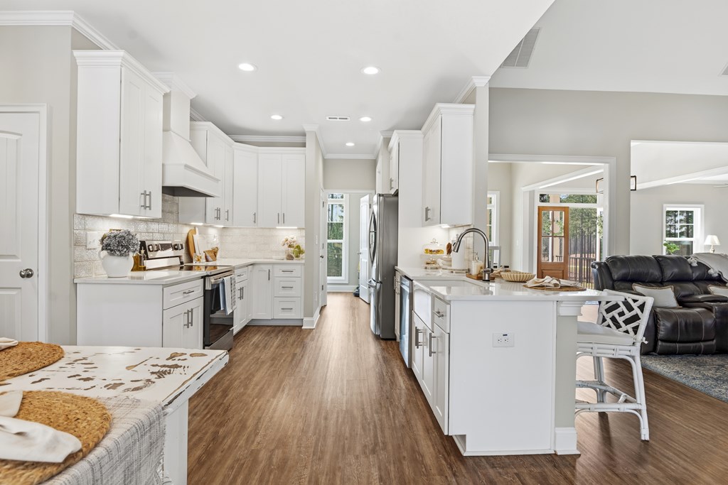 Open kitchen with white cabinets, a large island, stainless steel appliances, and wood floors.