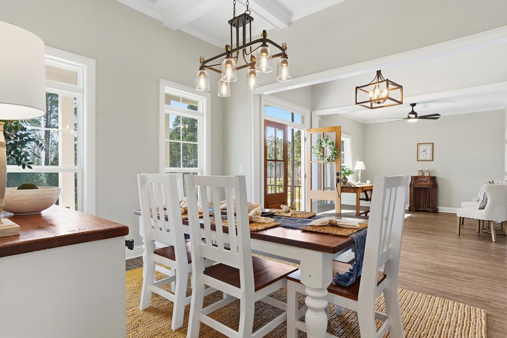 Dining area with a long wood-topped table, white chairs, and glass doors opening outside.
