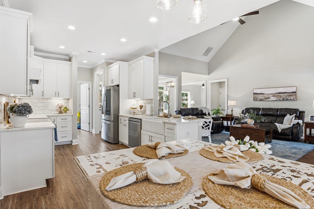 Open-plan kitchen and living room with white cabinetry, vaulted ceiling, and black leather seating.