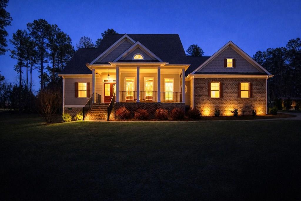 House at night with a lit columned porch, brick facade, and front lawn.