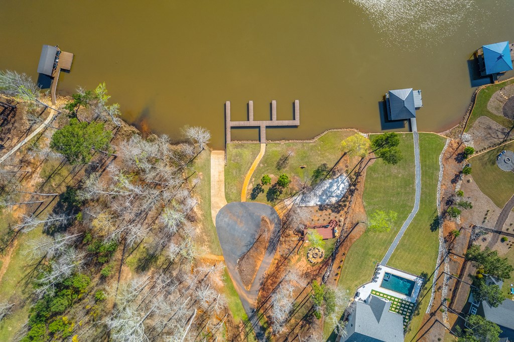 Aerial view of a lakefront property with a private dock, landscaped yard, and swimming pool.