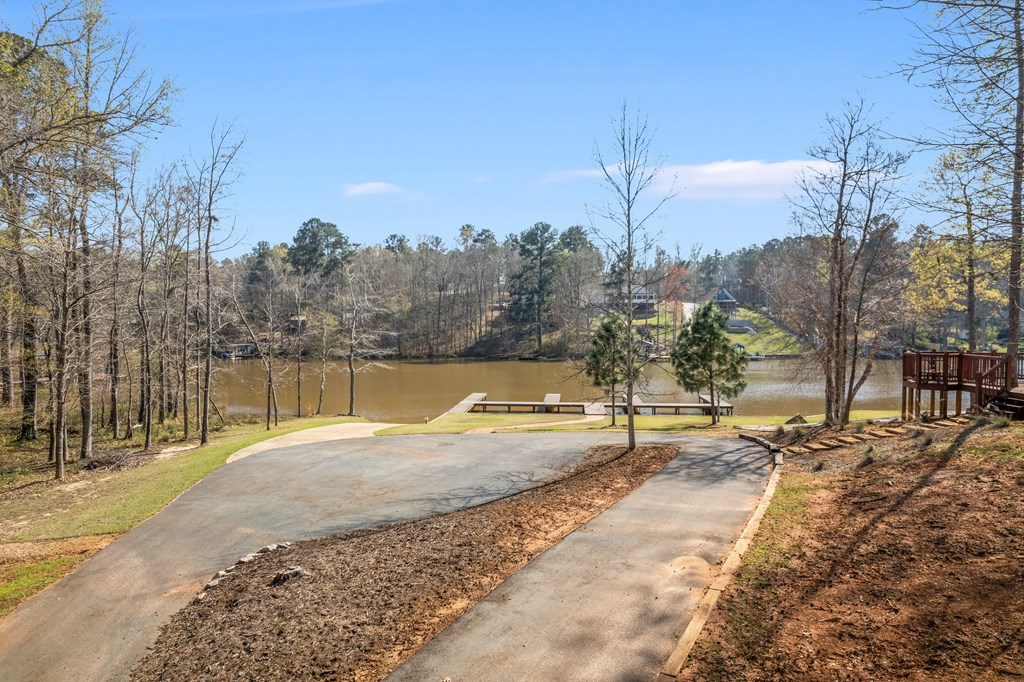 Paved driveway leading to a waterfront dock, with wooded banks across the water.