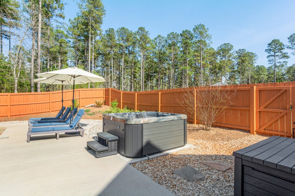Fenced backyard patio with a hot tub and umbrella-shaded lounge chairs.
