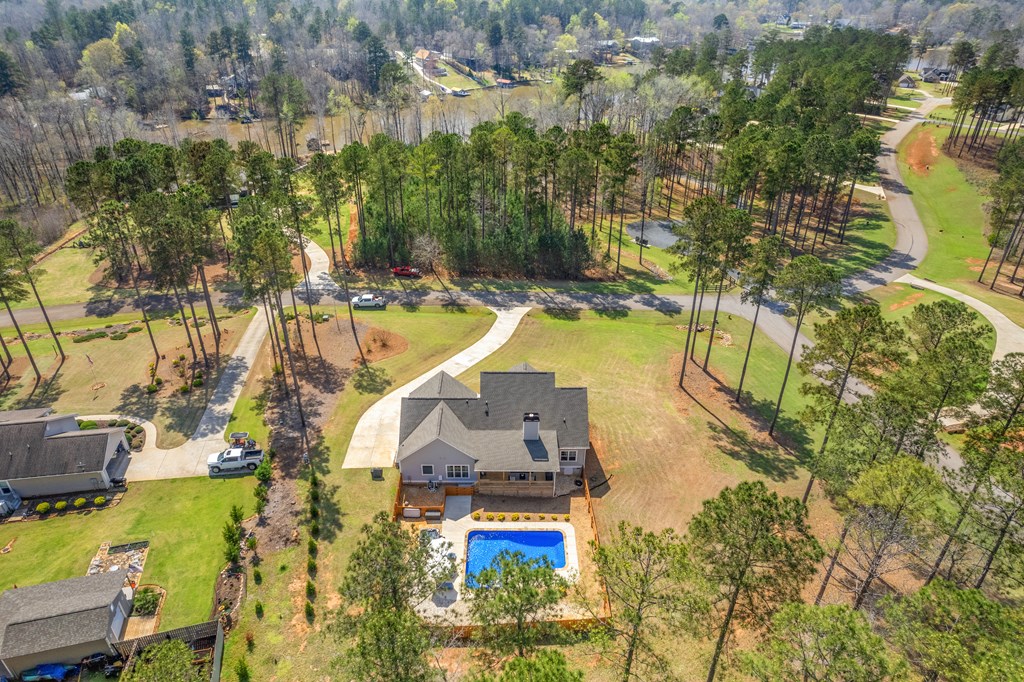 Aerial view of a house with a blue pool, broad lawn, and wooded surroundings.