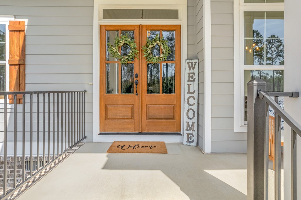 Covered front porch with wreath-decorated wooden double doors and a vertical welcome sign.