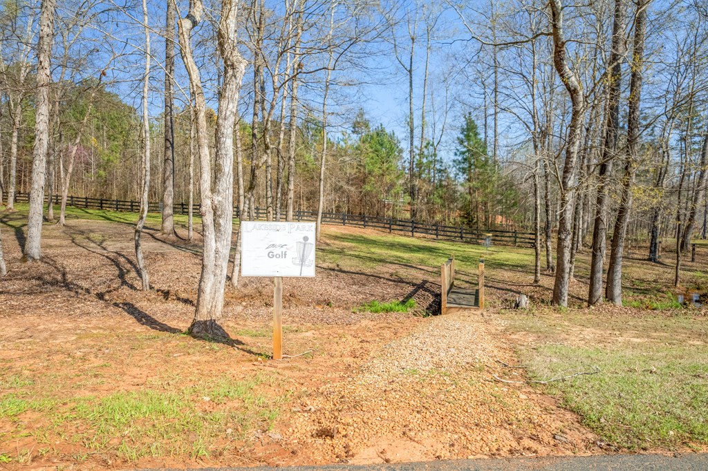 Wooded path at Lakeside Park Golf, with a sign beside the entrance and bare trees around it.
