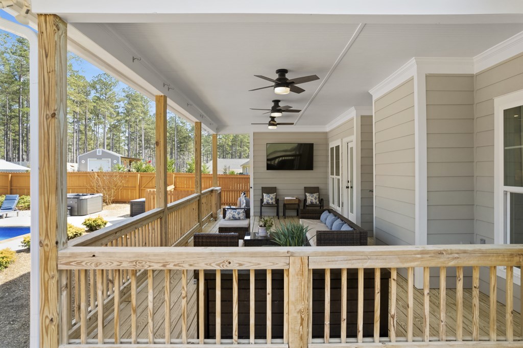 Covered porch with wicker seating, ceiling fans, and views of a fenced yard and pool.