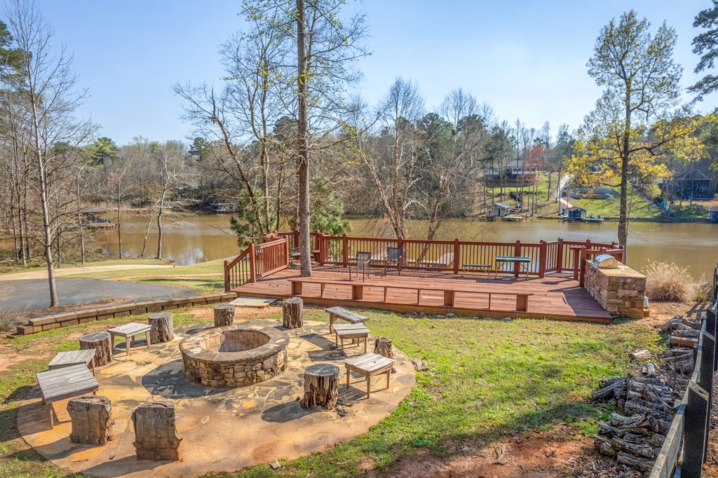 Lakeside backyard with a wooden deck and stone fire pit surrounded by stump seats.