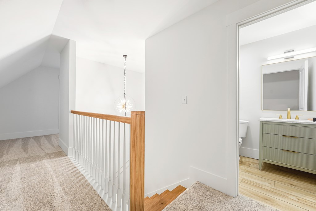 Upstairs landing with a wood-topped railing and view into a bathroom with a green vanity.