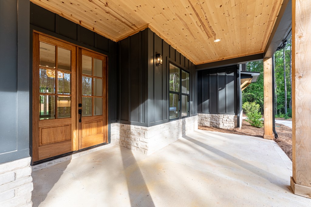 Covered front porch with a wood-plank ceiling, double entry doors, and dark siding over a stone base.