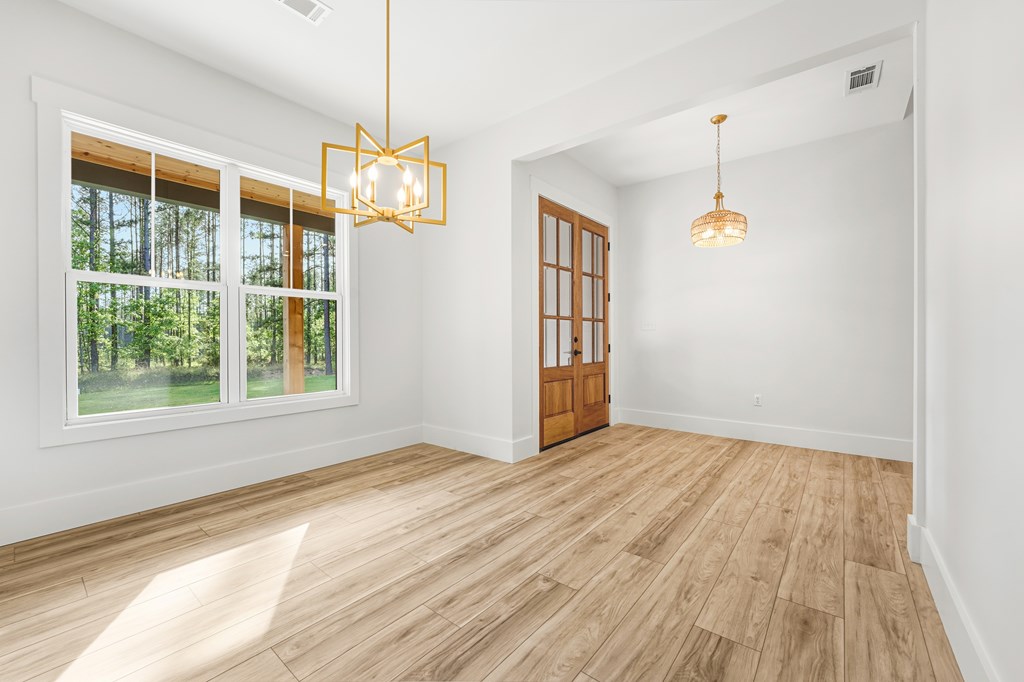Empty dining area with wood-look floors, large windows overlooking trees, and wood-and-glass French doors.