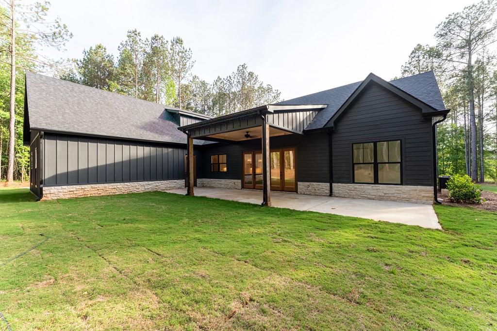 Dark-sided house with a covered rear patio and stone foundation, viewed across the lawn.
