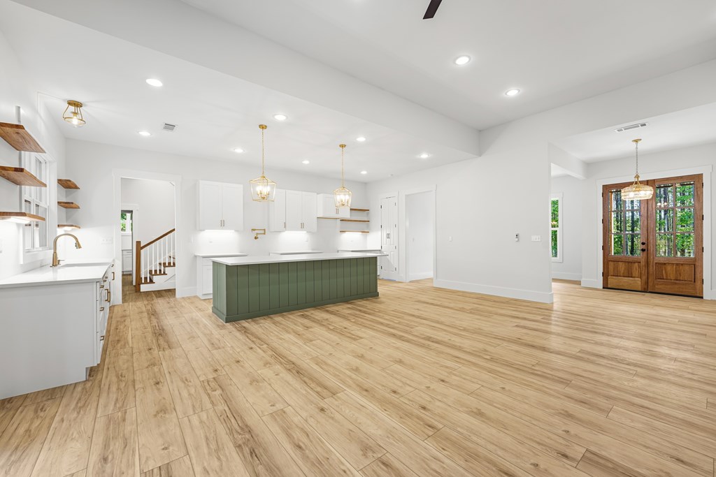 Spacious kitchen with a green island, white cabinets, light wood floors, and wooden glass-paneled doors.