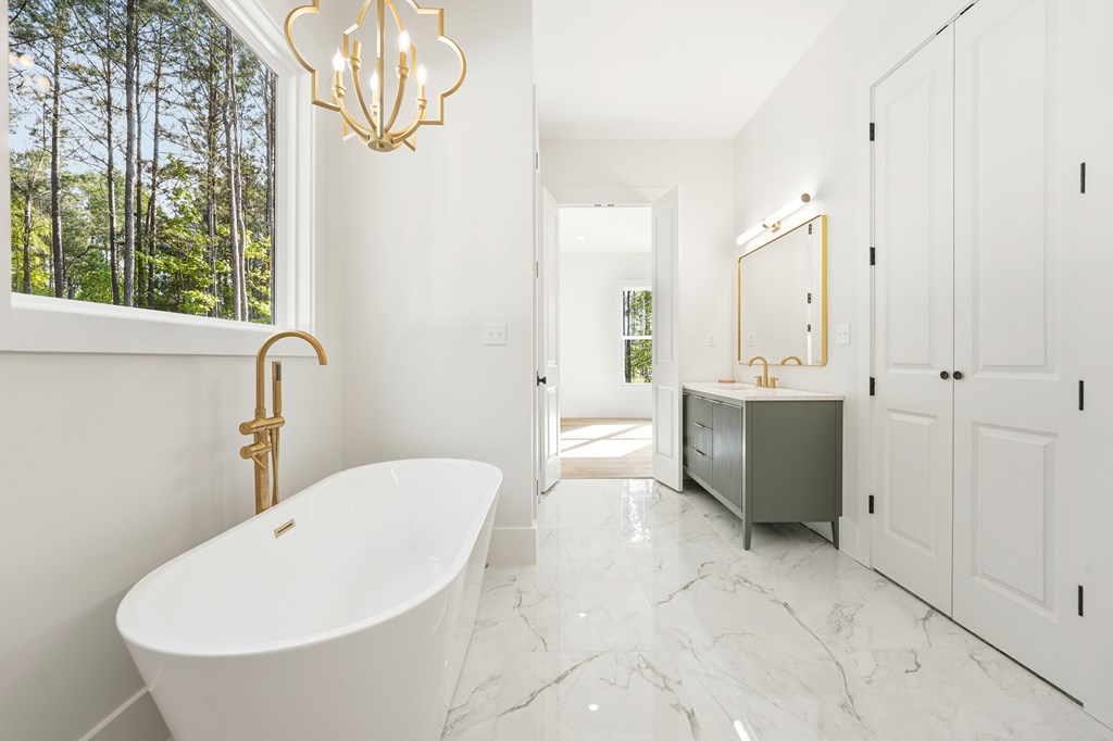 Bright bathroom with a freestanding soaking tub, brass fixtures, green vanity, and wooded view.