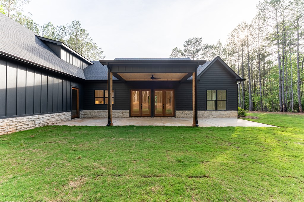 Modern dark-sided home with a covered patio and stone base, set beside a wooded lawn.