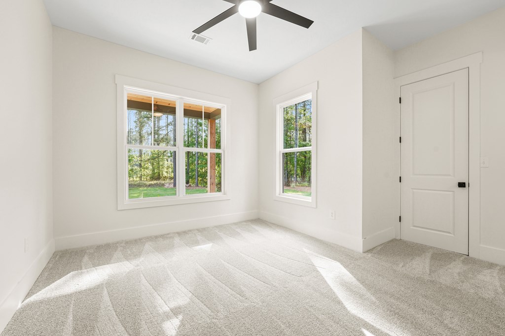 Vacant bedroom with carpet, a ceiling fan, and windows overlooking trees.