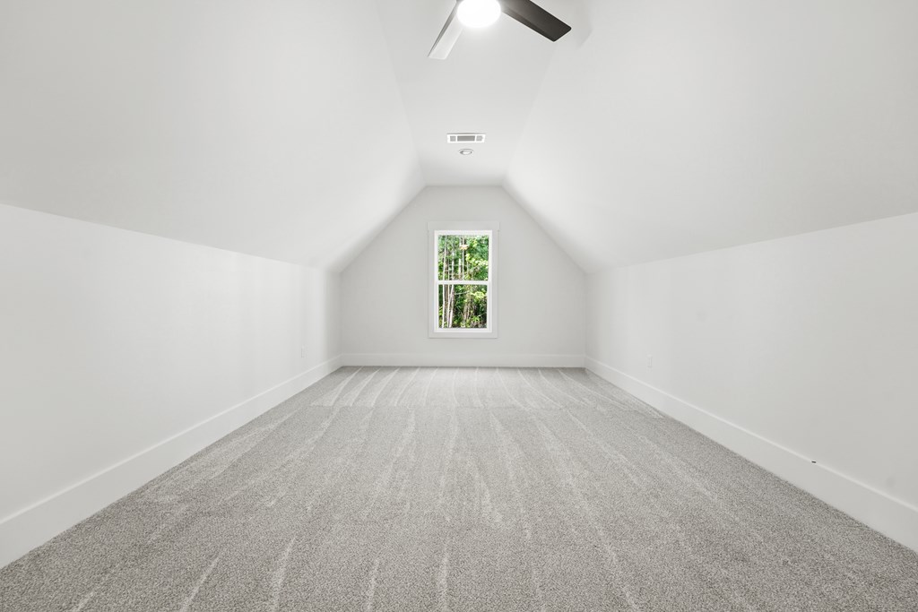 Finished attic room with sloped ceilings, gray carpet, and a window overlooking trees.