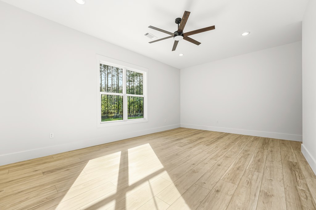Empty bright room with wood-look flooring, a dark ceiling fan, and a large window overlooking trees.