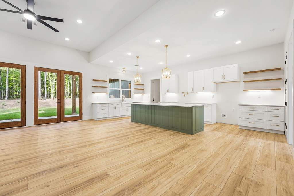Bright kitchen with a green island, white cabinets, wood floors, and glass doors to a wooded yard.
