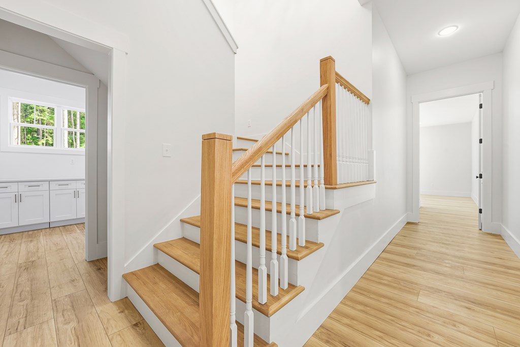 Staircase with light wood treads and handrail, white balusters, and matching flooring.