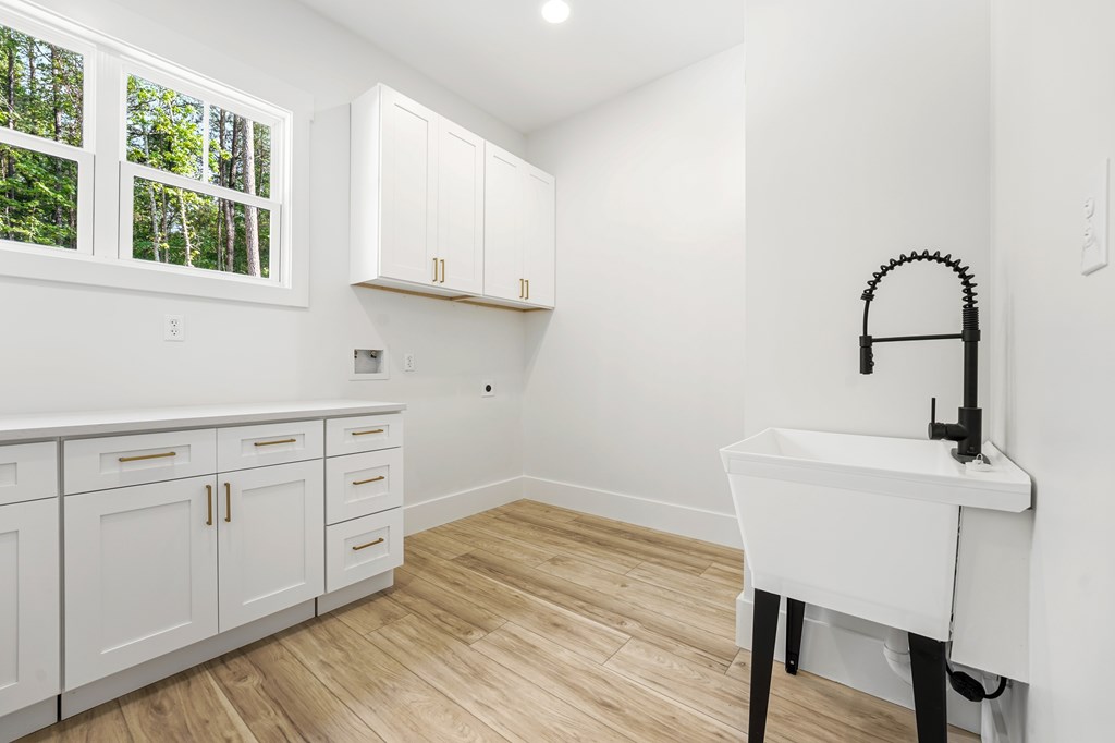 Bright laundry room with white cabinetry, large windows, wood-look flooring, and a deep utility sink.