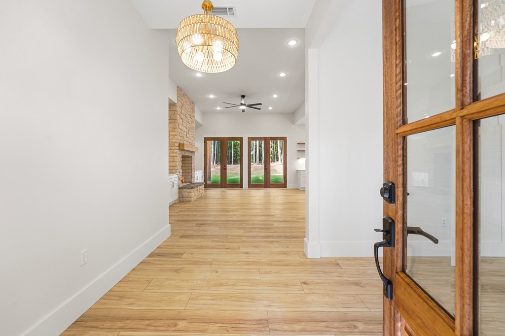Entry hall opening into a living area with wood floors, stone fireplace, and glass doors to the trees.