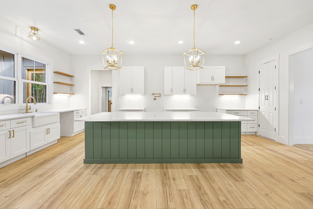Kitchen with a large dark green island, white cabinetry, and brass pendant lights.