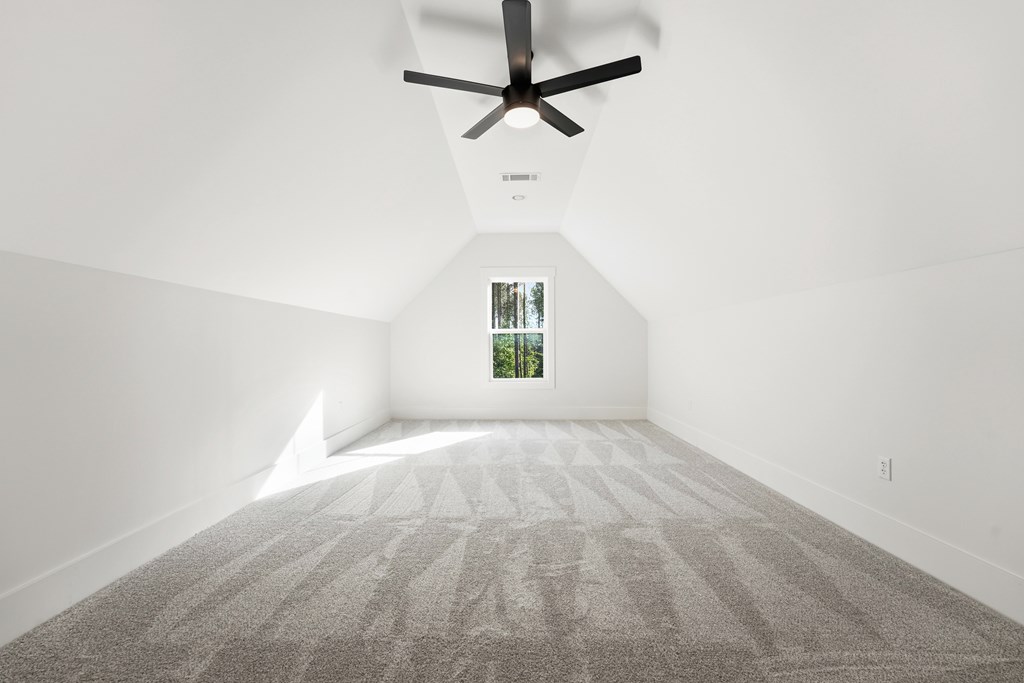 Vacant carpeted room with a vaulted ceiling, black ceiling fan, and window overlooking trees.