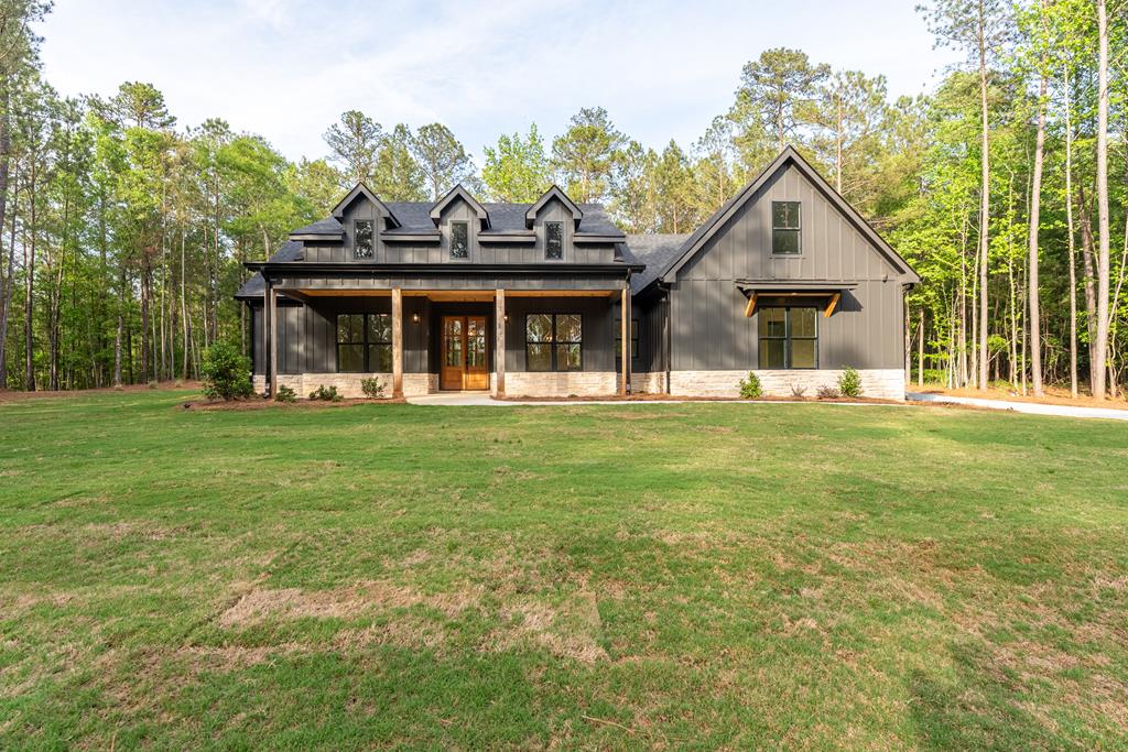 Dark gray house with a covered porch and dormers, surrounded by a lawn and trees.