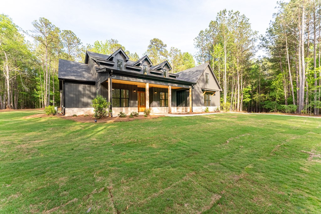 Dark gray farmhouse with a covered porch and gabled roof on a broad lawn surrounded by trees.