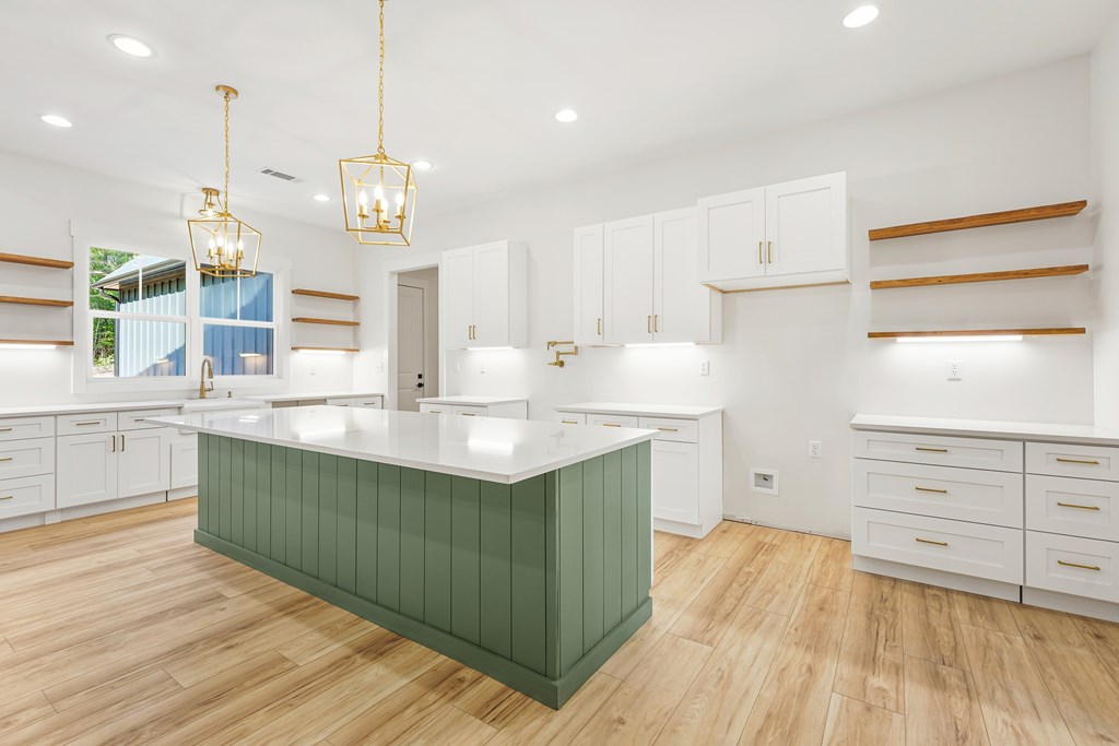 Kitchen with a large green island, white cabinetry, and brass pendant lights.
