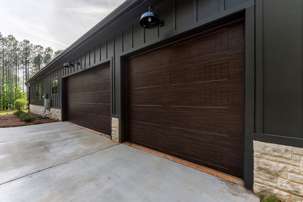 Home exterior with two dark wood-look garage doors, black lights, stone accents, and a concrete driveway.