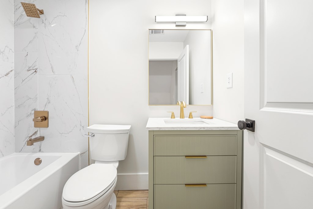 Bathroom with marble-look shower tile, a sage-green vanity, and brass fixtures.