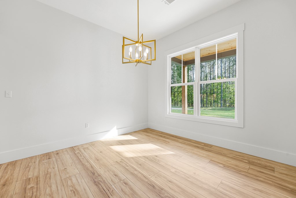 Vacant room with wood-look flooring, a gold chandelier, and a large window overlooking trees.