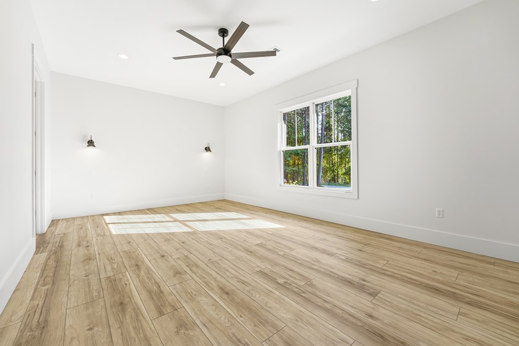 Vacant bedroom with wood-look flooring, a ceiling fan, and a window overlooking trees.