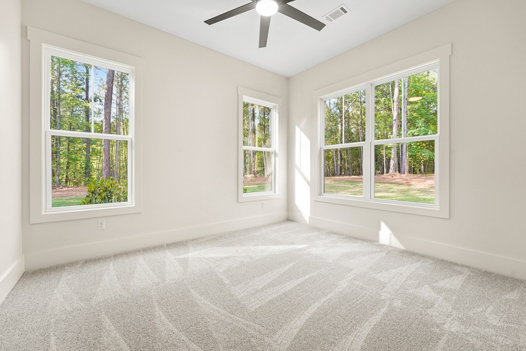 Empty carpeted bedroom with three large windows overlooking trees and a grassy yard.