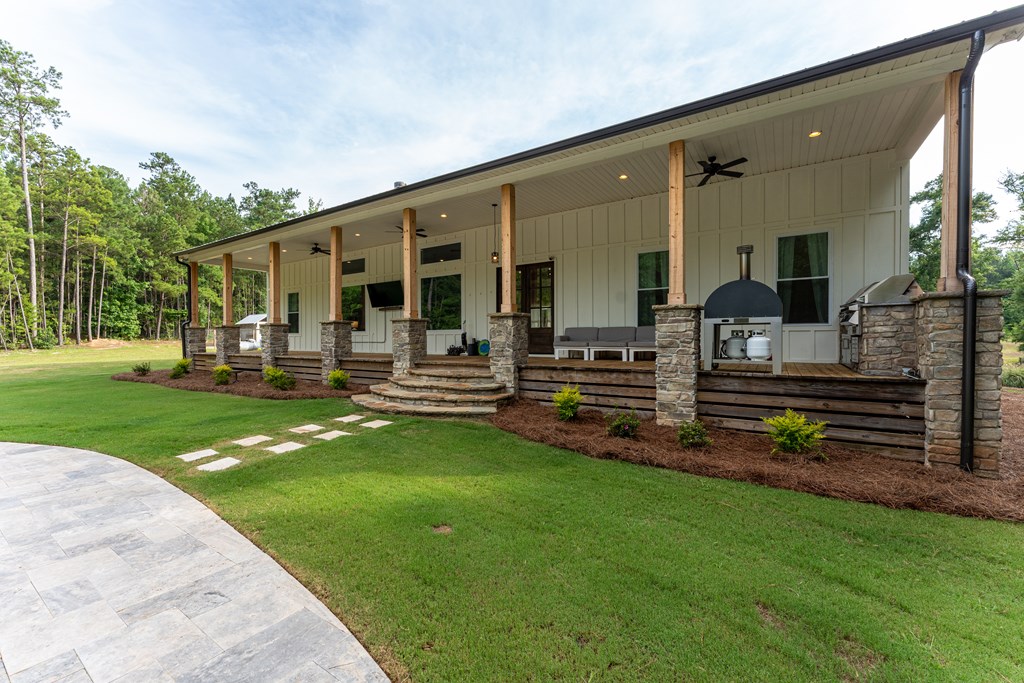 Covered porch with stone columns, outdoor seating, grill, and a manicured lawn.