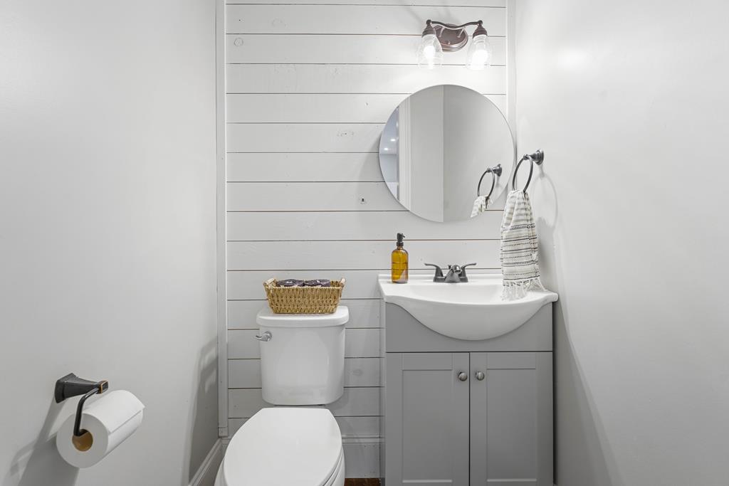 Bathroom with a gray vanity, round mirror, white shiplap wall, and toilet.