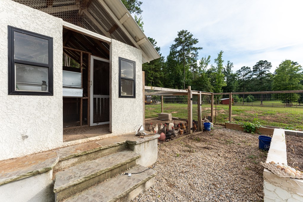 White chicken coop with stone steps and a fenced run where chickens gather.