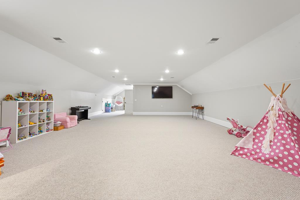 Spacious carpeted playroom with a pink teepee, toy shelves, and a wall-mounted TV.