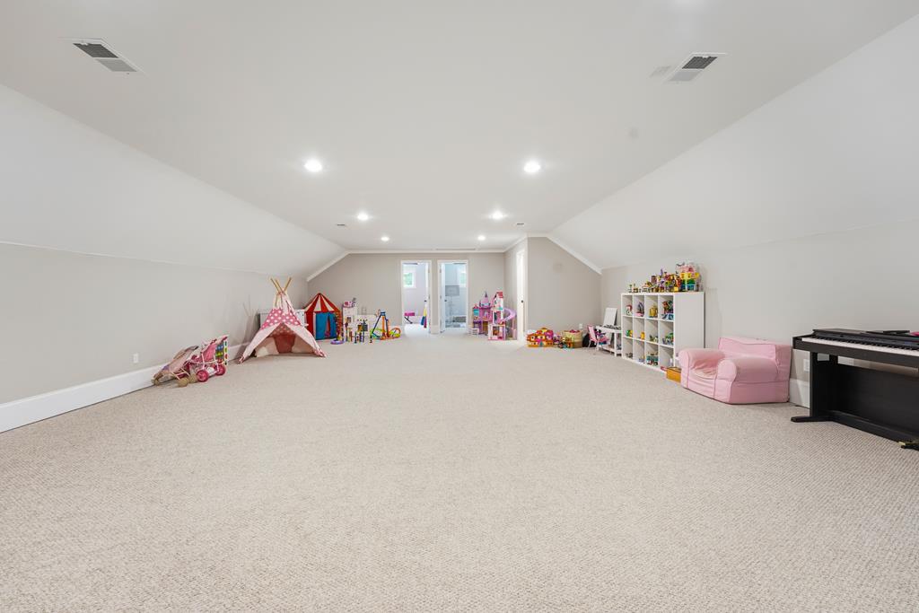 Carpeted playroom with toys, play tents, a pink chair, and a piano beneath a sloped ceiling.