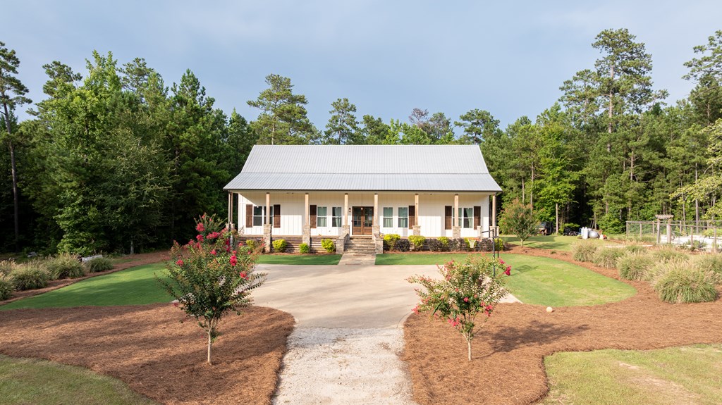 Single-story home with a covered porch and metal roof, set among trees at the end of a landscaped driveway.