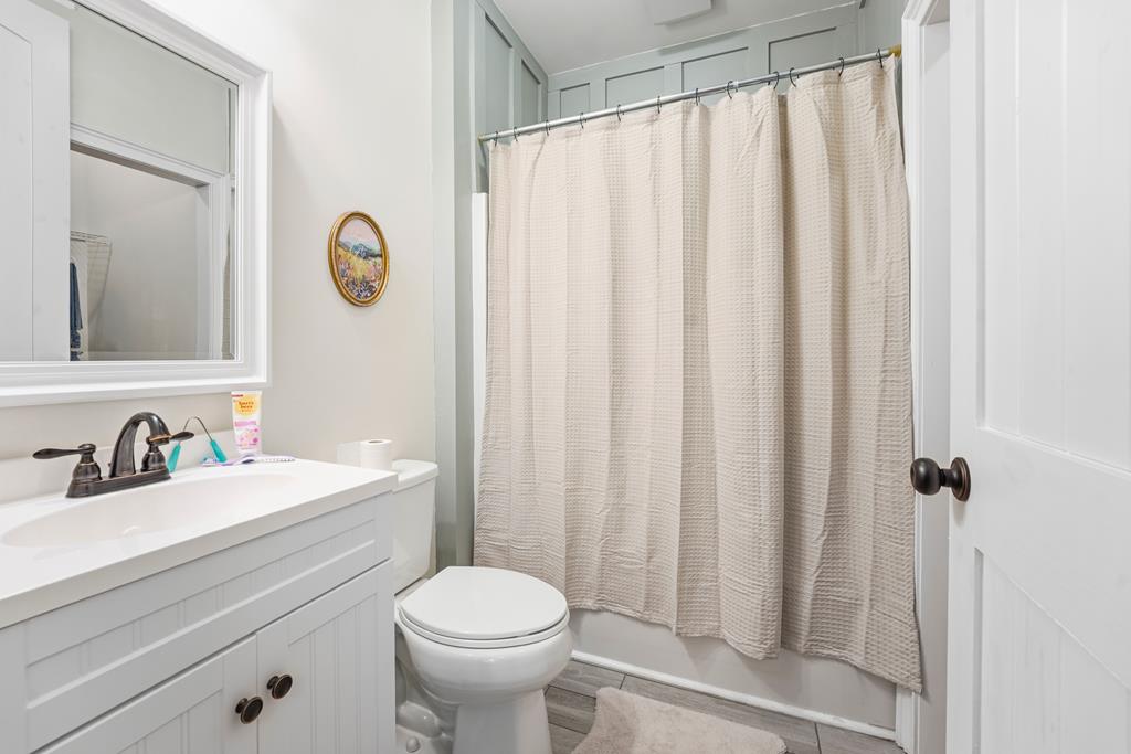 Bathroom with a white paneled vanity, toilet, and cream-curtained tub.