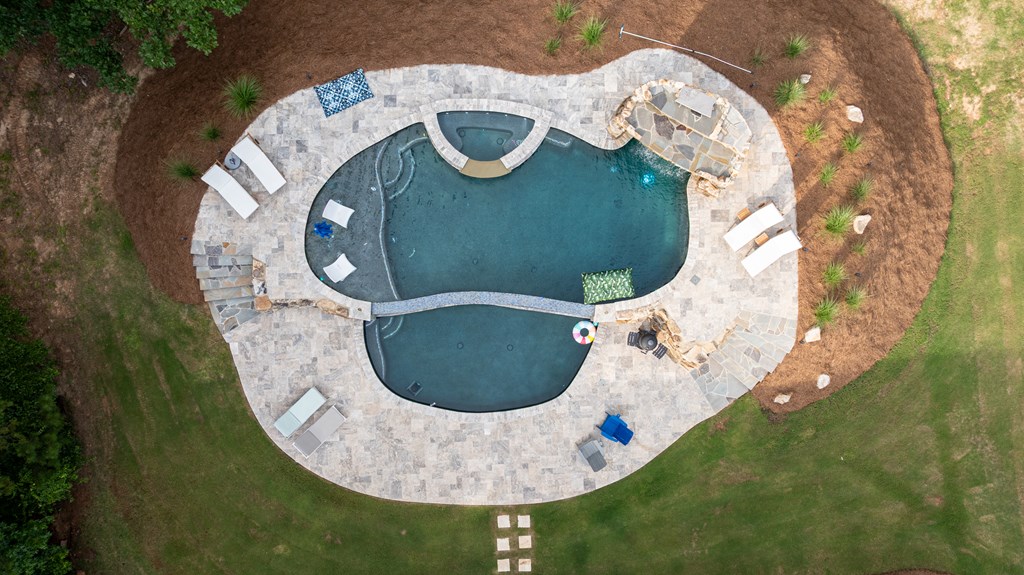 Aerial view of an irregular pool and connected spa on a stone patio with lounge chairs.