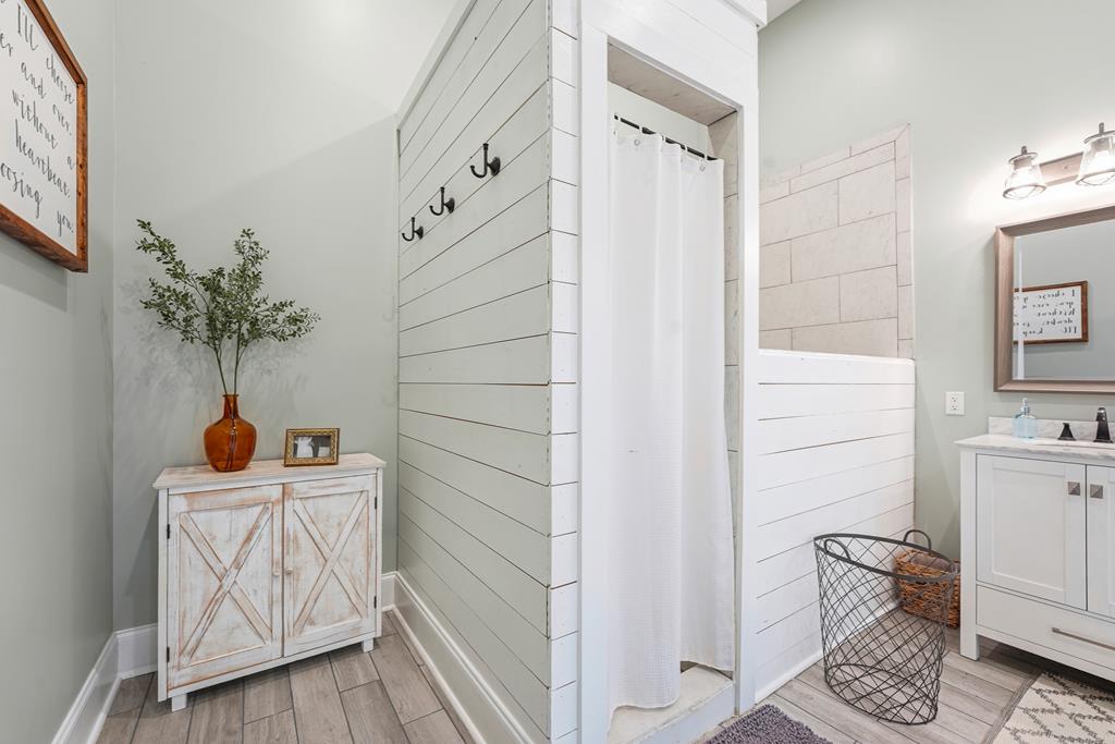 Bathroom with a white shower curtain, tiled wall, and distressed cabinet topped with a vase.