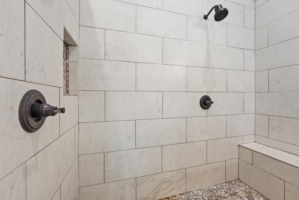 Tiled shower with dark bronze fixtures, a built-in bench, and pebble flooring.