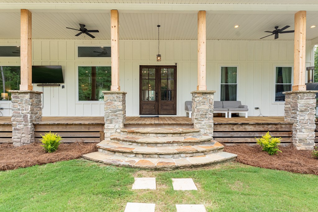 Covered porch with stone columns and curved stone steps leading to a lawn.