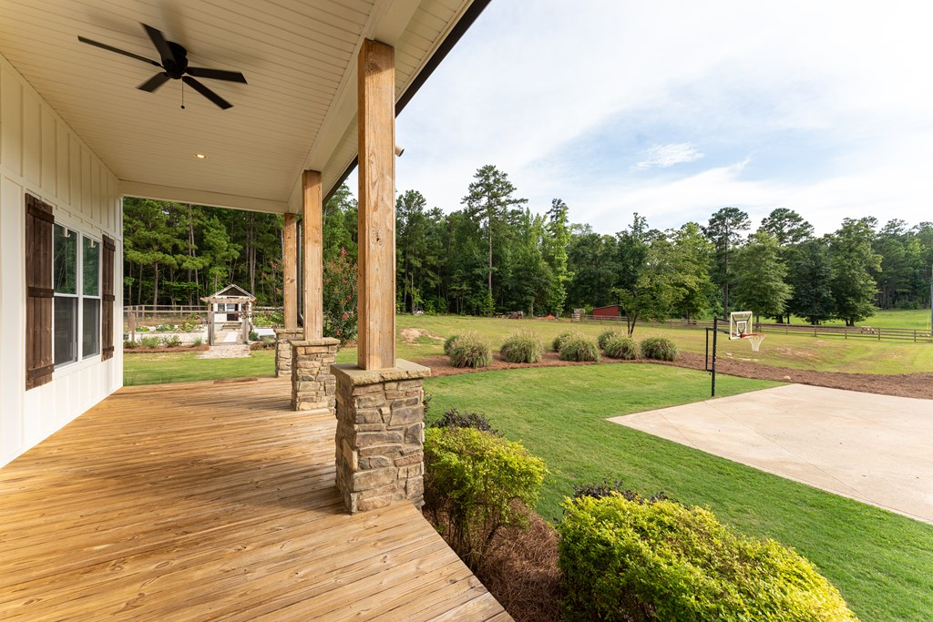 Covered wooden porch overlooking a landscaped lawn, basketball court, and wooded grounds.